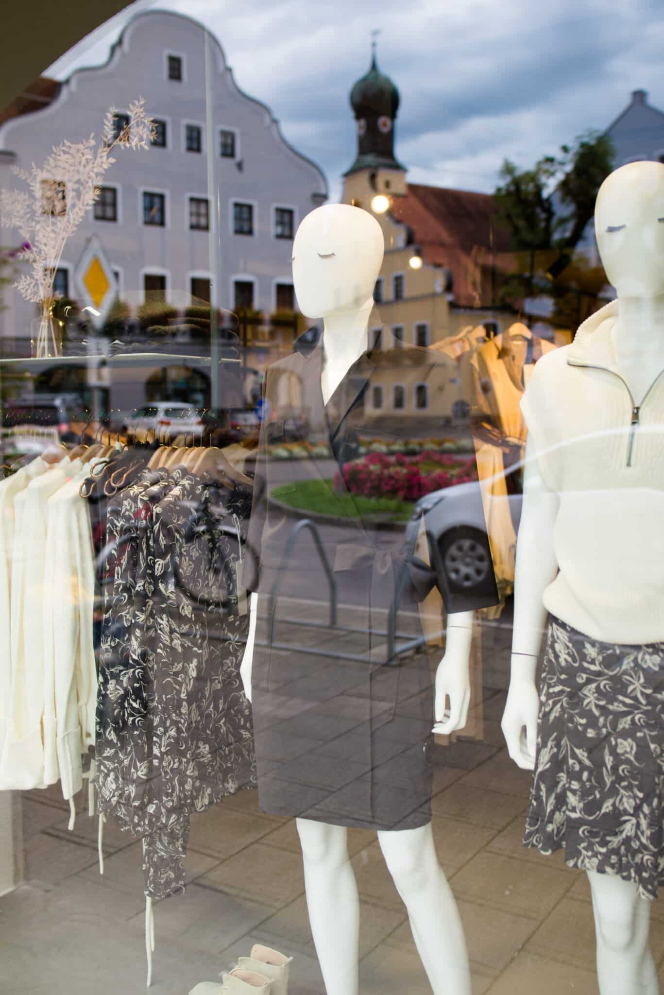 Obermaier Moden Schaufenster mit weißen und grauen Kleidungsstücken, Spiegelungen von Gebäuden und Straßen, urbane Innenstadt, 70er Stil der Fassaden