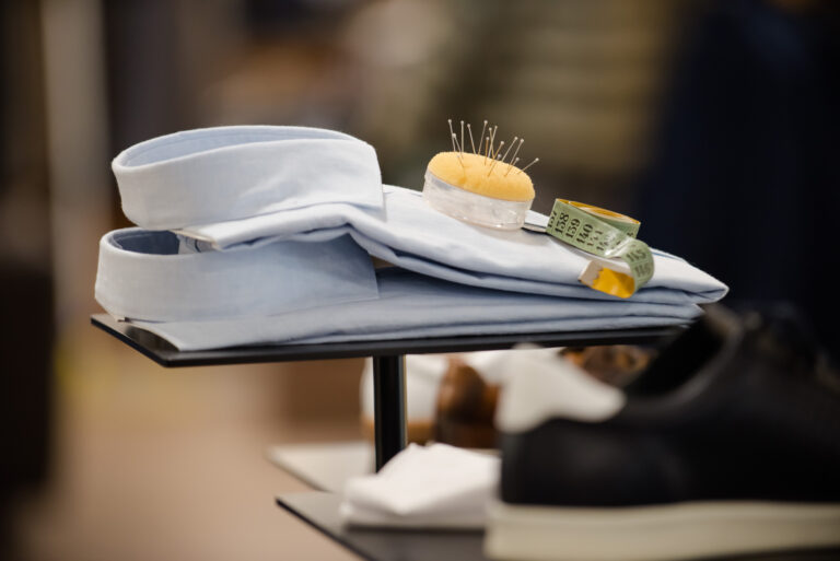 Blaues Hemd aus Baumwolle, ordentlich gefaltet, mit Maßband und Stecknadeln auf dem Tisch – Teil von Obermaier Moden, Service Fashion to pick zur Einkaufsbegleitung