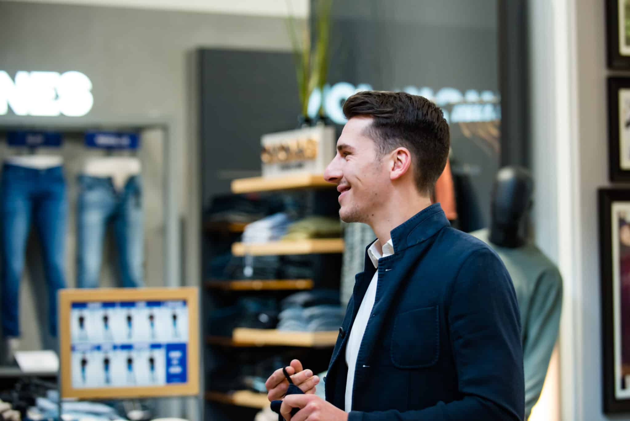 Seitenansicht eines Mannes in dunklem Jackett in einem Obermaier Moden Store, im Hintergrund Regale mit Kleidung